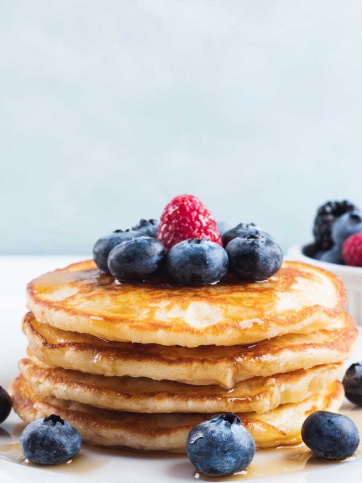 una pila de tortitas de yogur con miel y frutos rojos por encima