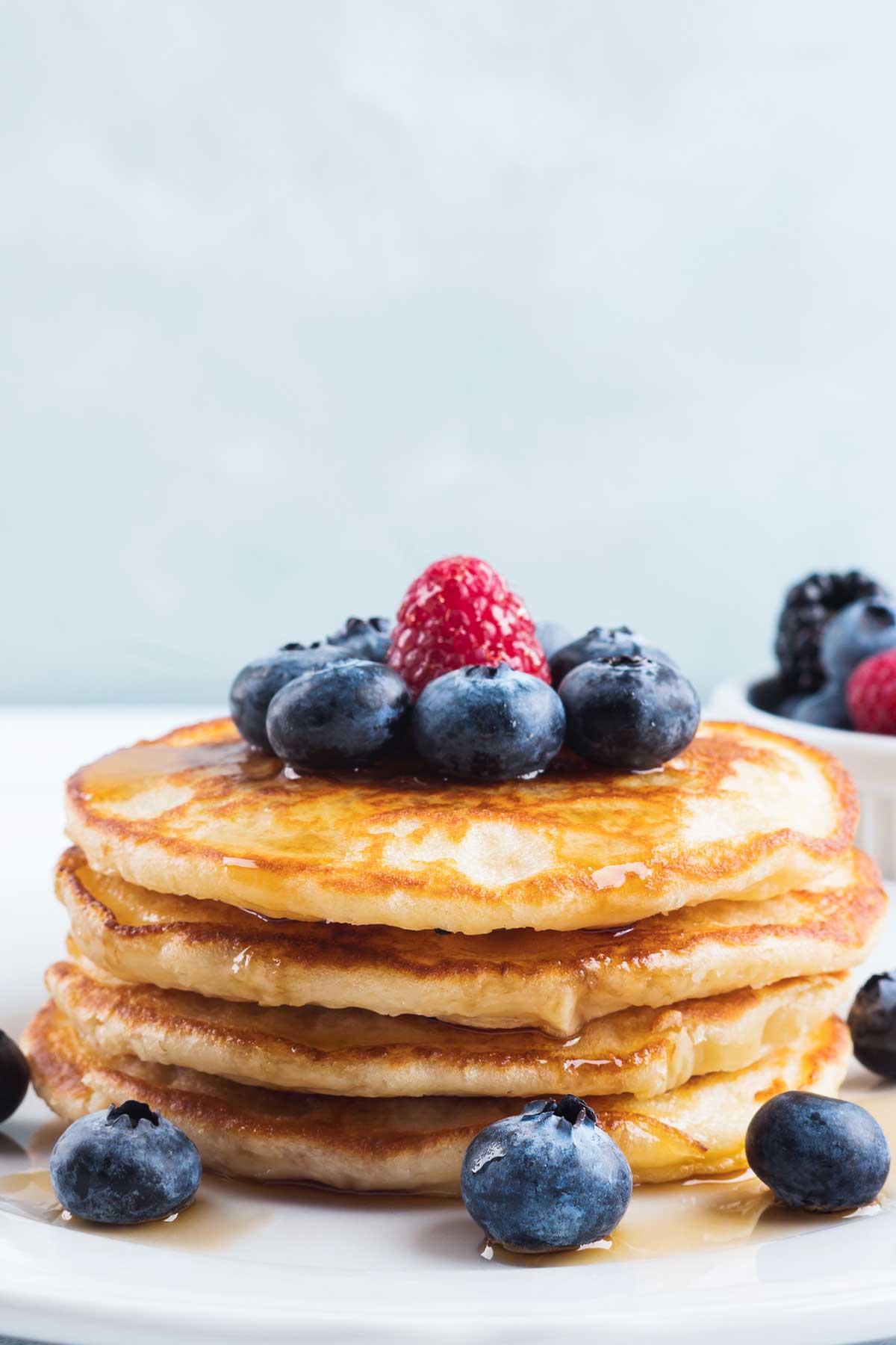 una pila de tortitas de yogur con miel y frutos rojos por encima