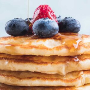 una pila de tortitas de yogur con miel y frutos rojos por encima