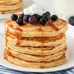 una pila de tortitas con arándanos y crema por encima