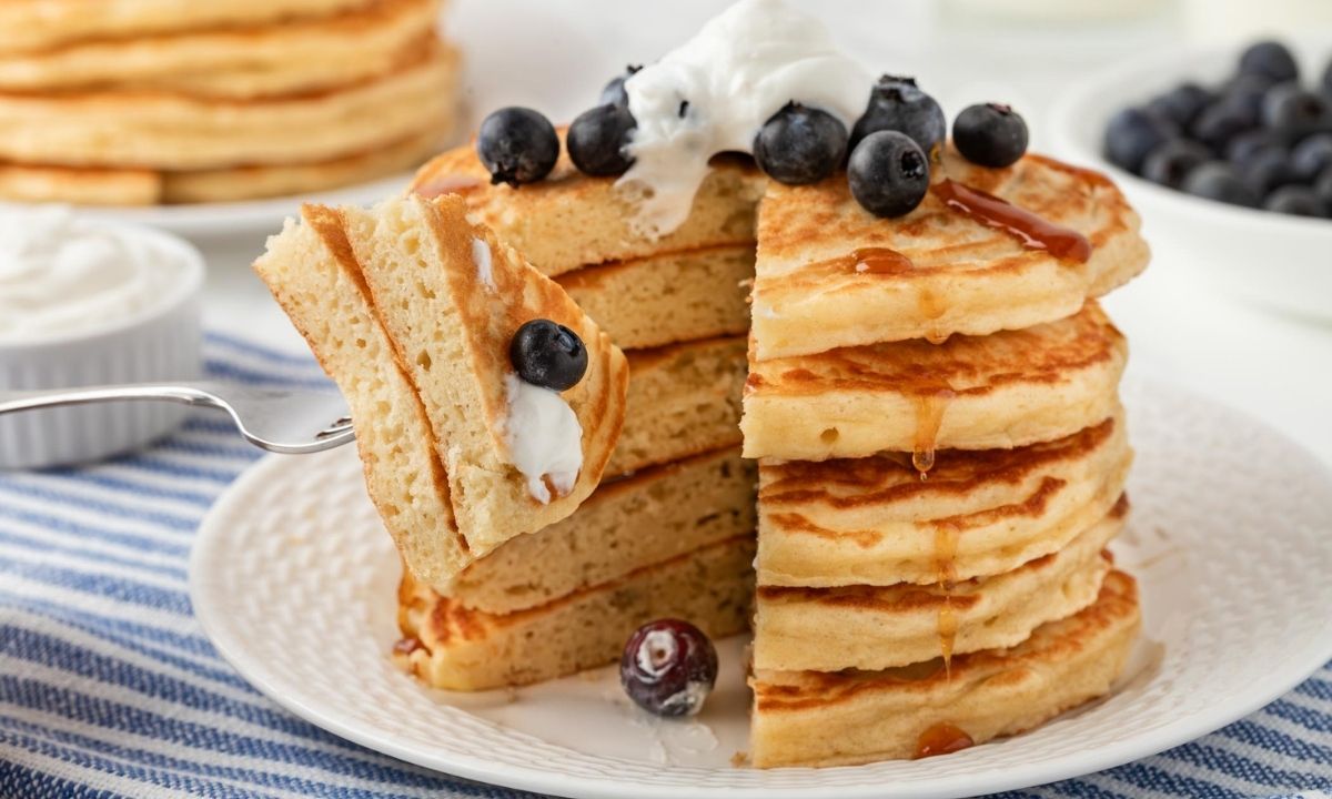 una pila de tortitas con arándanos y un tenedor pinchando una ración