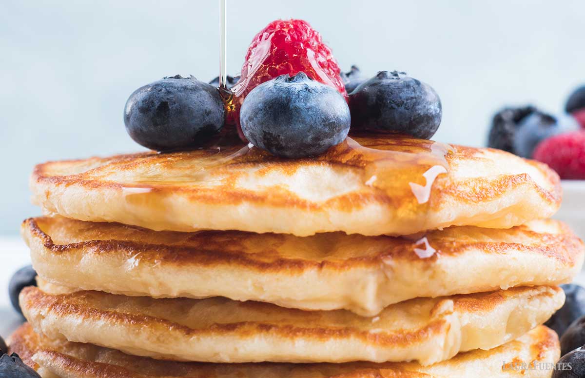 una pila de tortitas de yogur con miel y frutos rojos por encima