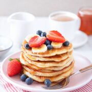 una pila de tortitas con plátano, fresas y arándanos encima