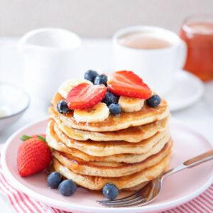 una pila de tortitas con plátano, fresas y arándanos encima