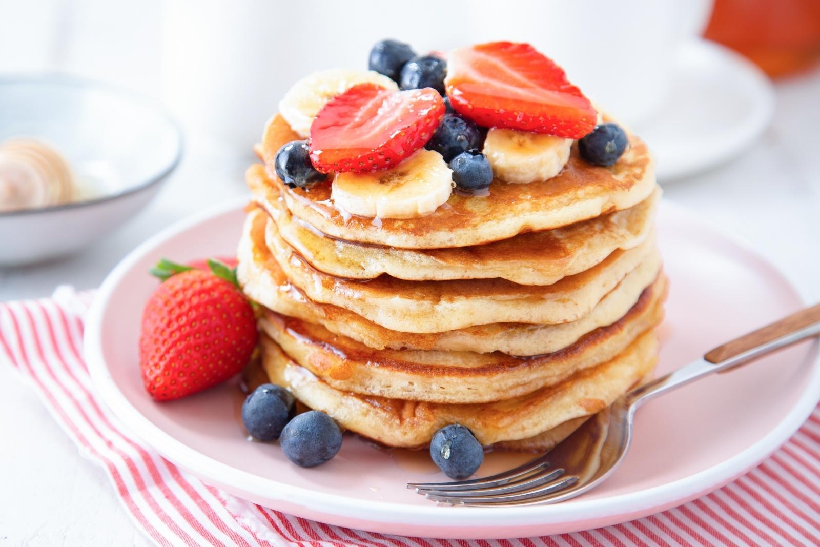 una pila de tortitas con plátano, fresas y arándanos encima