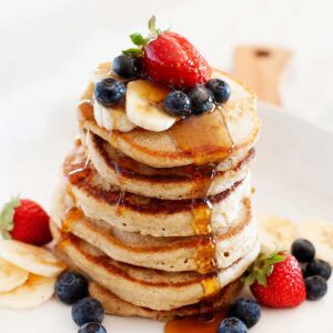 una pila de tortitas acompañadas con fresas, arándanos y rodajas de plátano