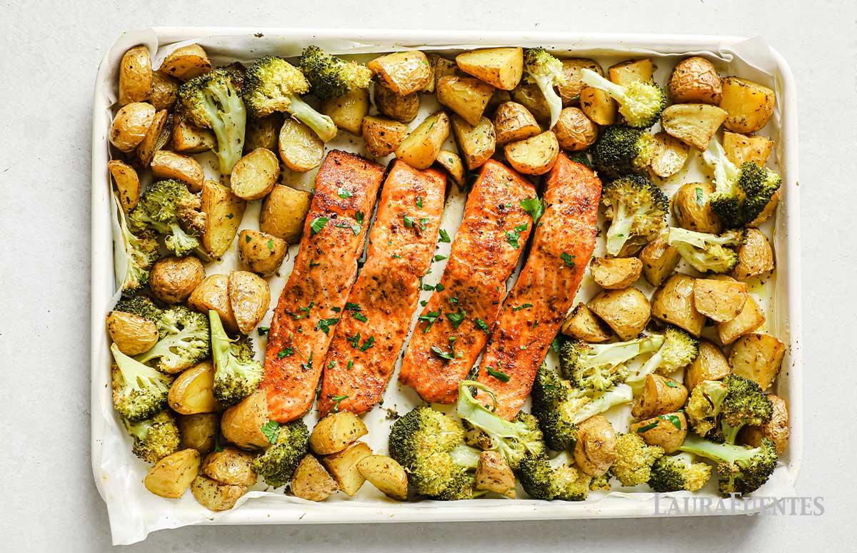 una bandeja para horno vista desde arriba, con filetes de salmón rodeados de patatas y brócoli 