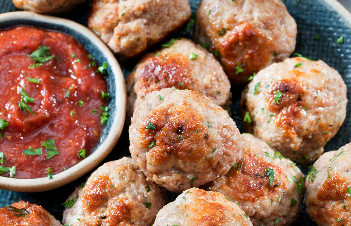 primer plano de albóndigas de pollo junto a un recipiente con salsa de tomate