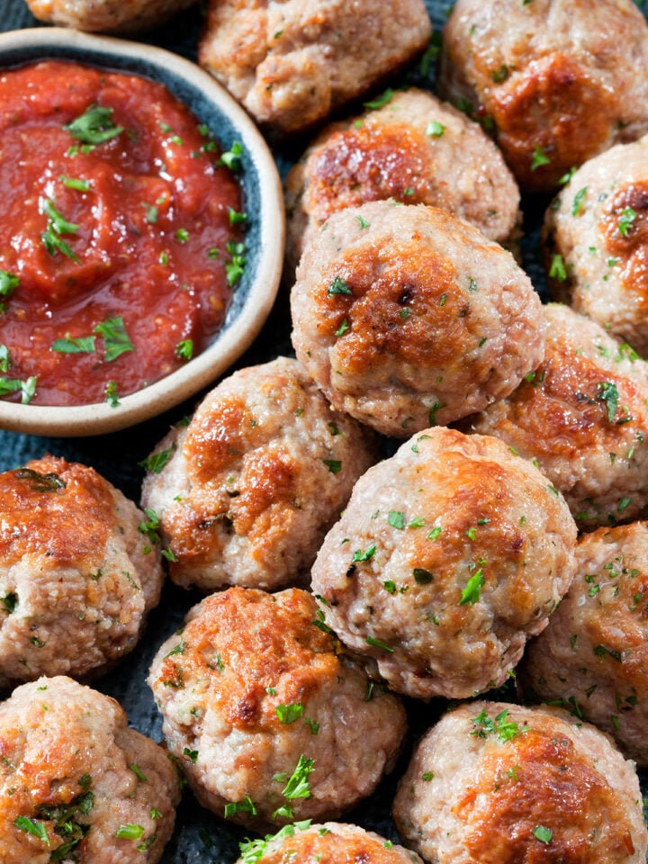 primer plano de albóndigas de pollo junto a un recipiente con salsa de tomate